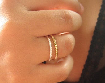 May include: Two thin, braided rings on a finger. One ring is gold and the other is silver.