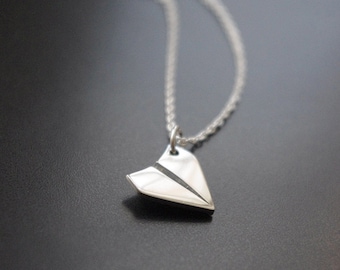 May include: A silver necklace with a paper airplane pendant. The chain is a delicate rope style.
