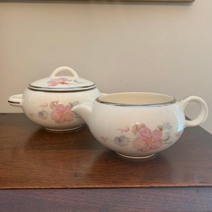 May include: A white creamer and sugar set with a floral design. The creamer and sugar are both decorated with pink flowers and a silver rim.
