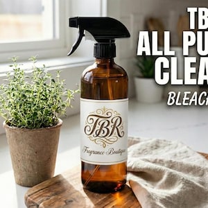 May include: A brown glass spray bottle labeled "TBR All Purpose Cleaner Bleach Free" sits on a wooden cutting board next to a small potted plant. The bottle has a black spray nozzle and a white label with gold lettering.