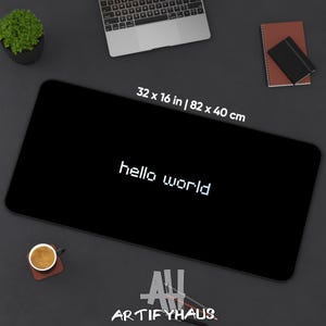 Könnte beinhalten: Eine rechteckige schwarze Schreibtischunterlage mit dem weißen, verpixelten Text hello world in der Mitte. Die Unterlage misst 82 x 40 cm. Das Design ist schlicht und einfach und bietet eine funktionale Oberfläche für Computerzubehör.