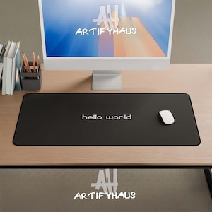 Peut inclure: Tapis de souris de bureau rectangulaire noir avec le texte "hello world" en blanc. Une souris d'ordinateur blanche est sur le côté droit du tapis. Un écran d'ordinateur et des accessoires de bureau sont en arrière-plan.