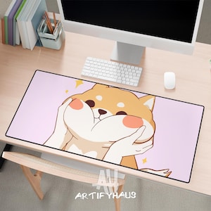 May include: A rectangular desk mat featuring a cartoon Shiba Inu dog with a surprised expression, holding its cheeks. The mat has a pink background and a black border. The text "ARTIFYHAUS" is at the bottom.