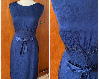 May include: A navy blue, sleeveless dress with a floral pattern. The dress features a satin bow at the waist and a beaded embellishment. The dress is displayed on a mannequin.