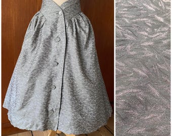 May include: A vintage gray skirt with a high, button-up waist and a subtle, textured pattern. The skirt has a flared silhouette and is displayed on a mannequin. The fabric has a slight sheen, adding to its vintage appeal.