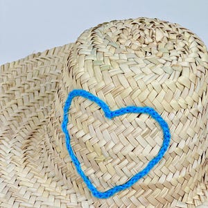 Puede incluir: Un sombrero de paja con un corazón azul bordado en la corona.