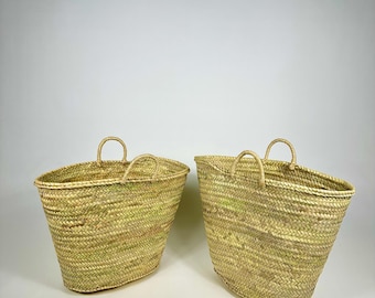 May include: Two large, natural woven baskets with handles. The baskets are made of a light brown, straw-like material and have a rounded, oval shape.
