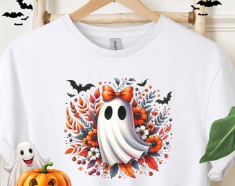 May include: White t-shirt featuring a cartoon ghost with a red bow, surrounded by orange and white flowers, leaves, and bats. The shirt has the word "White" printed on the bottom right.