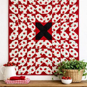 以下が含まれることがあります： 赤いイチゴ柄のキルトで、中央に黒いXがあり、木の棒に吊るされています。キルトは白い背景にイチゴの繰り返し模様が特徴です。木製のテーブルには、ピッチャー、ボウル、バスケットが置かれています。