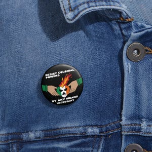 May include: A black button with the text "Resist Colonial Powers" and "By Any Means Necessary" around a burning heart with the Irish flag colours.