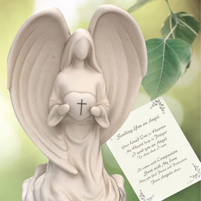 May include: White ceramic angel figurine holding a heart with a cross on it. The angel is sitting on a base and has wings. The figurine is accompanied by a card with the text "Sending You an Angel" and a poem about sending an angel to show that someone cares.