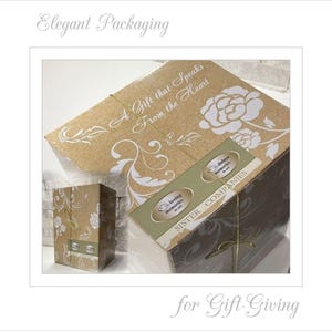 May include: A brown cardboard box with a floral design and the text "A Gift that Speaks From the Heart". The box is tied with a gold ribbon and has two labels that say "Loving Memories" and "Sister Companies".
