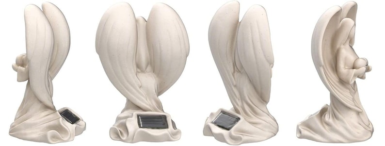 May include: White ceramic angel statue with wings outstretched, holding a small child in its arms. The statue has a solar panel on the base and is designed for outdoor use.