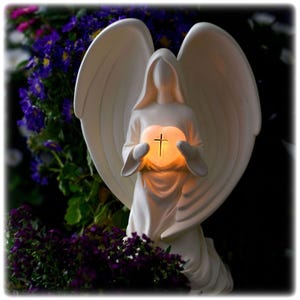 May include: White angel figurine with wings holding a heart with a cross inside. The heart is illuminated with a warm glow.