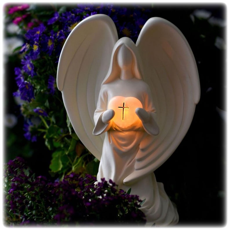 May include: White angel figurine with wings holding a heart with a cross inside. The heart is illuminated with a warm glow.