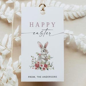 Peut inclure: Une étiquette cadeau de Pâques rectangulaire avec une illustration de lapin et les mots "HAPPY Easter" en écriture cursive. L'étiquette est ornée d'un pompon doré et d'une fougère. Le bas de l'étiquette indique "FROM, THE ANDERSONS".