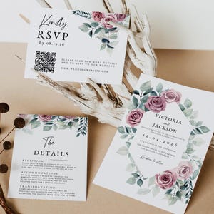 May include: A wedding invitation suite featuring three white cards with watercolour dusty rose flowers and green leaves. The cards display text including "Kindly RSVP," "The DETAILS," and "VICTORIA and JACKSON" with a QR code and event information.