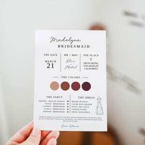Könnte beinhalten: Eine Einladungskarte für eine Brautjungfer mit dem Namen "Madelyne". Die Karte enthält Datum, Ort, Farben, Party-Mitglieder und Kleiderdetails. Das Farbschema umfasst Braun- und Burgundertöne. Die Karte wird von einer Hand gehalten.