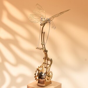 Puede incluir: Una escultura mec&aacute;nica de mariposa de color lat&oacute;n con intrincados engranajes y una base de madera. Las alas de la mariposa son delicadas y detalladas, con una est&eacute;tica steampunk. Los engranajes son visibles y a&ntilde;aden dise&ntilde;o.