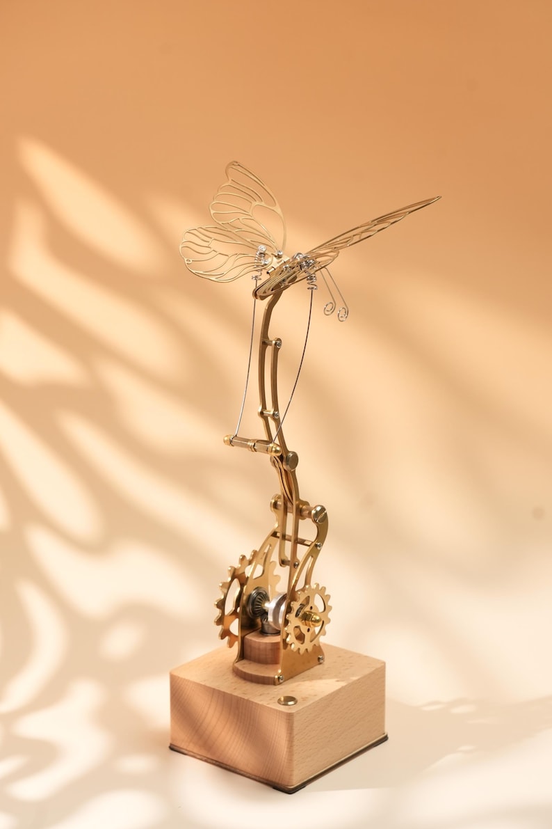 Puede incluir: Una escultura mec&aacute;nica de mariposa de color lat&oacute;n con intrincados engranajes y una base de madera. Las alas de la mariposa son delicadas y detalladas, con una est&eacute;tica steampunk. Los engranajes son visibles y a&ntilde;aden dise&ntilde;o.