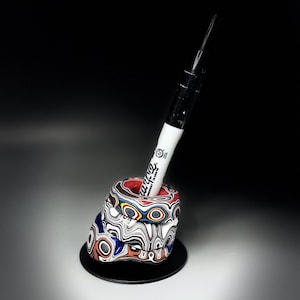 May include: A pen holder featuring a stack of three rings with a multi-colored marbled pattern in red, white, blue, and black. A black and white Sharpie marker is inserted into the center opening of the top ring, resting at an angle.