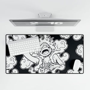 Puede incluir: Alfombrilla de ratón rectangular negra con una ilustración blanca de un personaje con la boca abierta, rodeado de formas de nubes. Un teclado y un ratón blancos están sobre la alfombrilla. Un monitor de ordenador está encima.