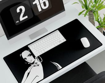 Puede incluir: Alfombrilla de escritorio rectangular negra con una ilustración blanca de la cara de una mujer. Un teclado y un ratón blancos están sobre la alfombrilla. Un monitor de ordenador muestra la hora 14:16. Una planta verde está en el fondo.