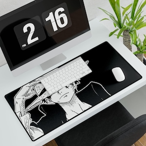 May include: Black desk mat with a white anime character illustration. A white keyboard and mouse sit on the mat, with a computer monitor showing the time. A plant is in the background.