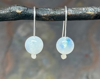 May include: A pair of silver dangle earrings with a white moonstone bead on each earring.
