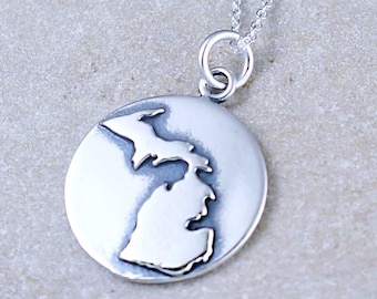 May include: A silver necklace with a round pendant featuring an outline of the state of Michigan. The pendant is attached to a silver chain.