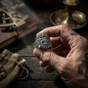 up of a rugged man's hand holding a heavy stainless steel Tláloc Aztec ring, showcasing the chunky Mesoamerican tribal face design.