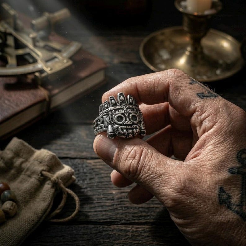 up of a rugged man's hand holding a heavy stainless steel Tláloc Aztec ring, showcasing the chunky Mesoamerican tribal face design.