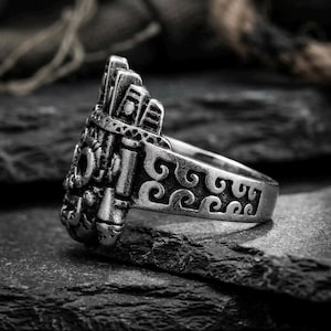 Side profile of a thick stainless steel ancient history ring showing deep geometric wave engravings on dark slate rock.