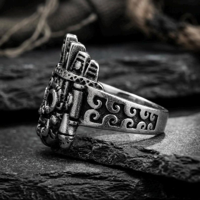 Side profile of a thick stainless steel ancient history ring showing deep geometric wave engravings on dark slate rock.