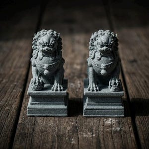 May include: A pair of grey stone guardian lion statues, each featuring intricate manes, collars with bells, and seated on rectangular pedestals. One lion rests a paw on a textured sphere, while the other rests a paw on a small cub figure.