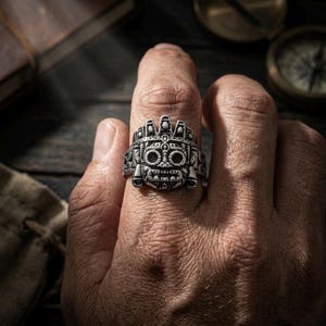 Close up of a rugged man's hand wearing a thick silver Aztec mythology men's statement ring to show true scale and size.