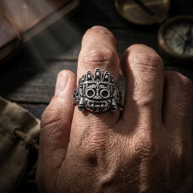 Close up of a rugged man's hand wearing a thick silver Aztec mythology men's statement ring to show true scale and size.