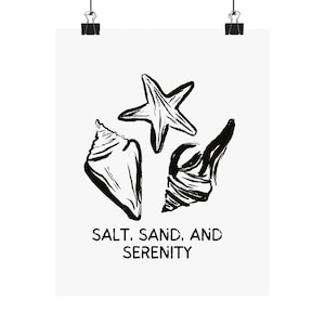 May include: Black and white art print featuring a starfish and two seashells. The text "SALT, SAND, AND SERENITY" is printed below the illustrations. The print is held by two black binder clips.