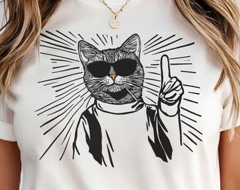 May include: White t-shirt with a black and white illustration of a cat wearing sunglasses and pointing upwards. The cat has a cigarette in its mouth and is surrounded by radiating lines.