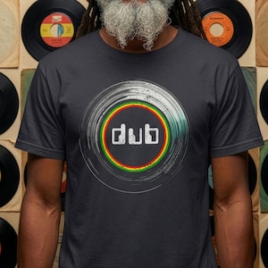 Puede incluir: Camiseta gris oscuro con un diseño circular con la palabra "dub" en letras blancas. El diseño incorpora una combinación de colores verde, amarillo y rojo, que se asemeja a un disco de vinilo. Una prenda informal.