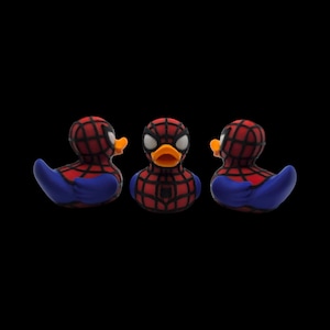 以下が含まれることがあります： スパイダーマンに似せてデザインされた3つのラバーダック。アヒルの頭と背中には赤と黒のクモの巣模様、青い翼、オレンジ色のくちばしがあります。スパイダーマンのロゴは、中央のアヒルの胸に表示されています。