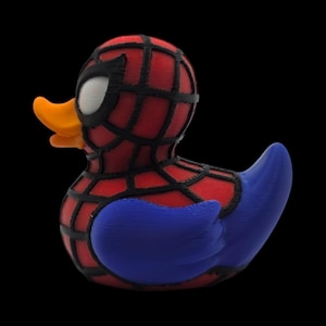 以下が含まれることがあります： スパイダーマン風のノベルティラバーダック。赤いボディに黒いウェブのディテール、青い翼、オレンジ色のくちばし、スパイダーマンのマスクデザインが特徴です。背景は黒です。