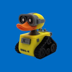 May include: A yellow and gray 3D-printed figure of a duck-like robot, with an orange beak and goggles. The robot has black treads and the text "WALL-E" on the side. The background is a solid blue.