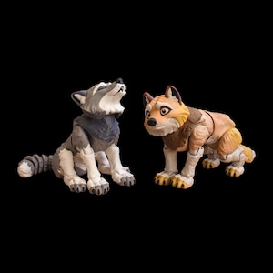 May include: Two articulated wolf figurines. One is gray and white, looking upward. The other is tan, brown, and yellow, with a curious expression. Both are posed on a black background.