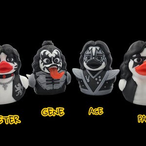 May include: Four rubber duck figurines styled after the members of the rock band KISS. Each duck has black hair, face paint, and a red beak. The names "PETER", "GENE", "ACE", and "PAUL" are written below each duck in yellow.
