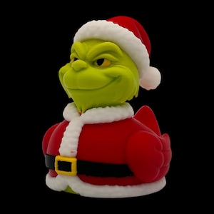 May include: A green character figurine wearing a Santa Claus hat and red coat with white trim. The figurine has a black belt with a gold buckle. The background is solid black.