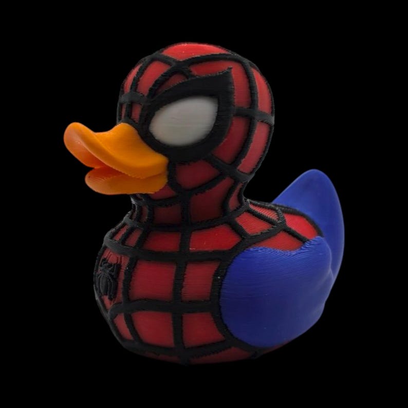 以下が含まれることがあります： スパイダーマン風のノベルティラバーダック。アヒルは赤と黒のウェブマスク、白い目、オレンジ色のくちばしが特徴です。体は赤で黒のウェブと青い翼が付いています。胸には小さなクモのエンブレムが付いています。