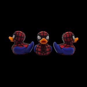 以下が含まれることがあります： スパイダーマン風のラバーダック3羽。頭と胴体に赤と黒のクモの巣模様、青い翼、オレンジ色のくちばしが特徴です。中央のダックの胸にはスパイダーマンのロゴが見えます。