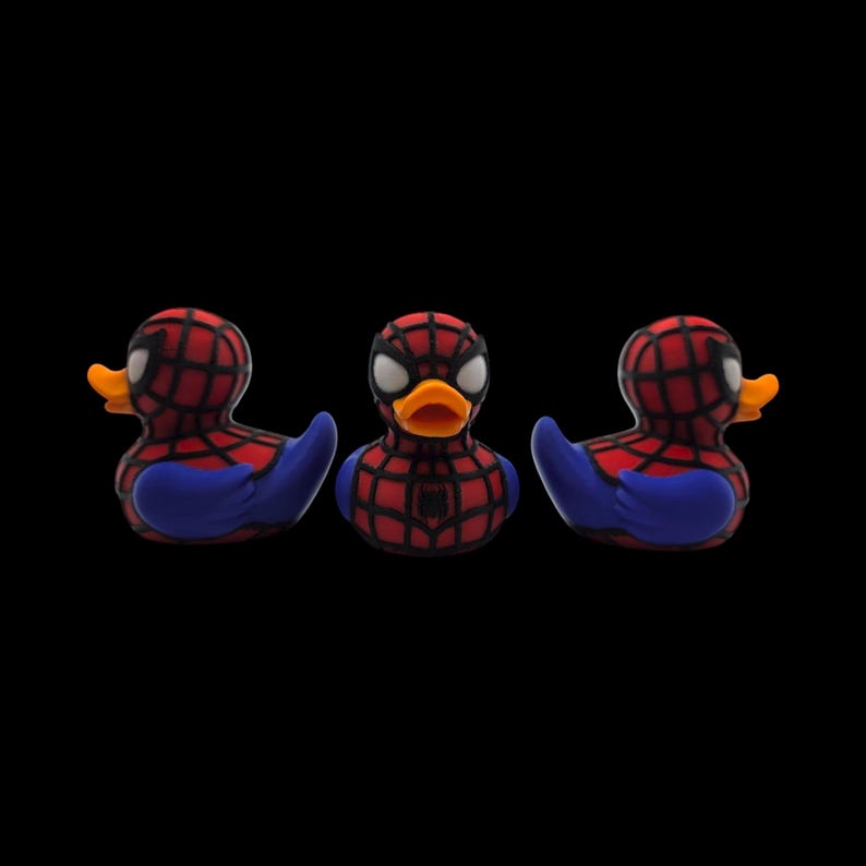 以下が含まれることがあります： スパイダーマン風のラバーダック3羽。頭と胴体に赤と黒のクモの巣模様、青い翼、オレンジ色のくちばしが特徴です。中央のダックの胸にはスパイダーマンのロゴが見えます。