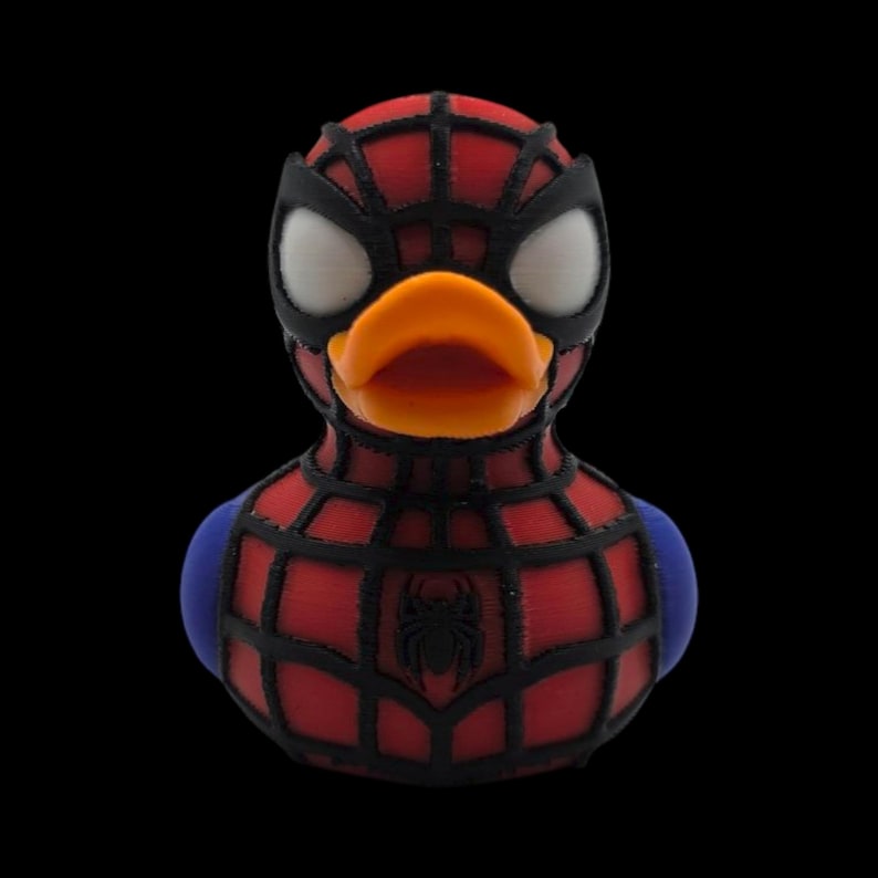 以下が含まれることがあります： スパイダーマン風のラバーダック。赤と黒のウェブスーツ、黒いマスク、白い目。オレンジ色のくちばしと青い肩のアクセントがあり、胸にはクモのエンブレムが付いています。